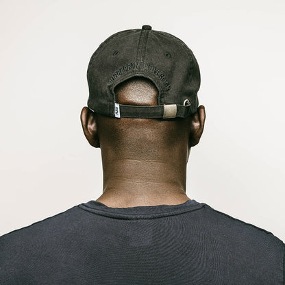 The back profile of a young male model with a shaved head, wearing a black, one-size-fits-all 6-panel cap, made of 100% cotton. The back of the cap features the brand name "RUBBERBAND SOVEREIGN" also embroidered in black, situated above the cap's adjustable opening and a RSG woven loop label. The cap is secured with a metal clasp closure, allowing for a customizable fit and the unstructured, low-profile design gives the cap a relaxed and comfortable fit.