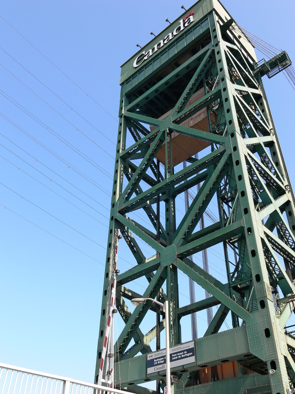 An upward view of the Hamilton Harbors' towering green steel structure of a bridge lift mechanism with 'Canada' written at the top, showcasing industrial engineering against a clear blue sky.