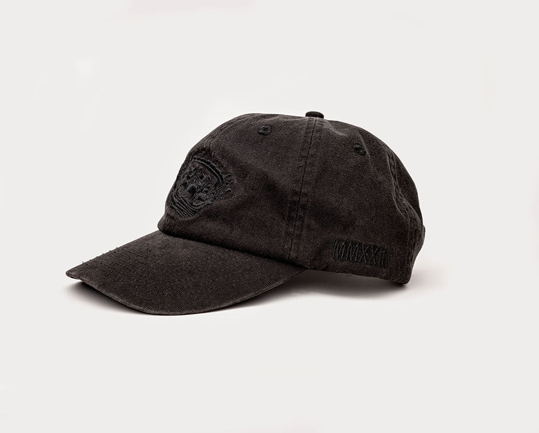 A black coloured, one-size-fits-all 6-panel cap, made of 100% cotton, featuring the left side  of the cap showing the Roman Numerals for "2023" in black embroidery. 